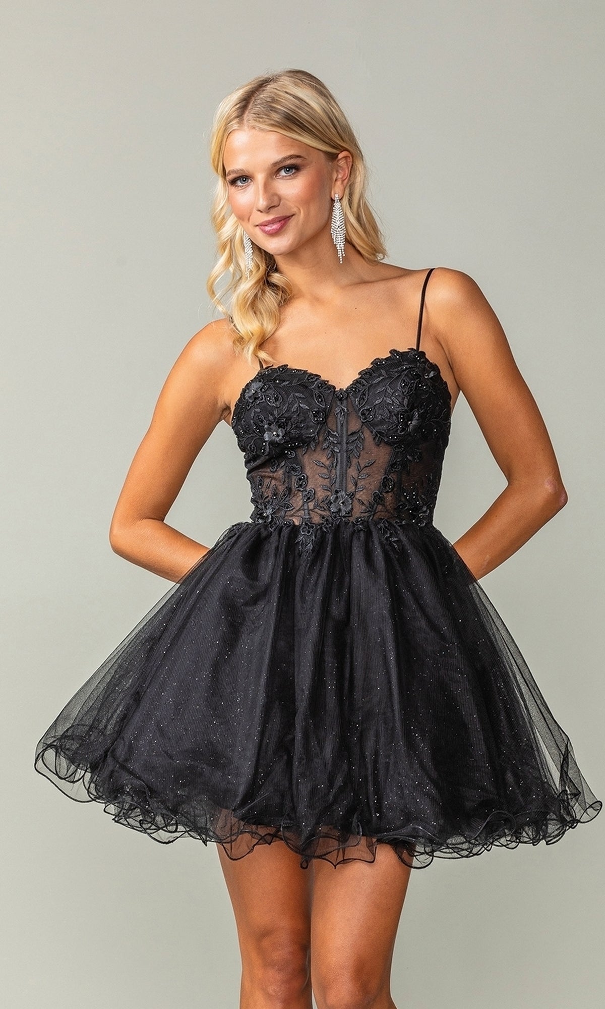A woman wears the Sheer-Waist Short Babydoll Homecoming Dress 3382, featuring a fitted floral lace bodice and voluminous tulle skirt, as she poses against a plain background.